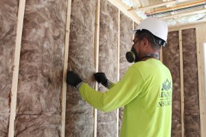 An Advanced Green worker installs fiberglass insulation on a building wall